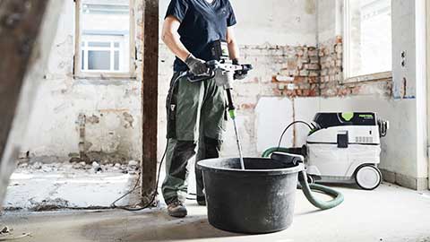 Eine Handwerkerin steht in der Baustelle und verwendet einen Festool Rührer in Kombination mit einem Sauger