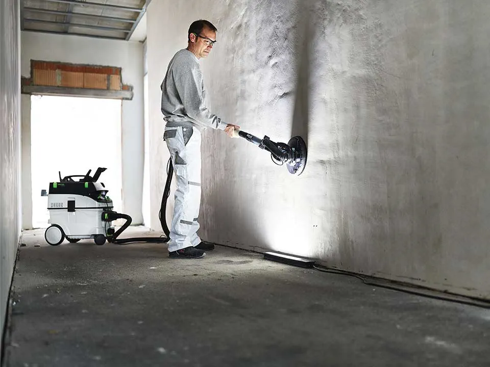 Ein Handwerker leuchtet mithilfe des Maler-Streiflichts eine Wand aus und schleift diese ab