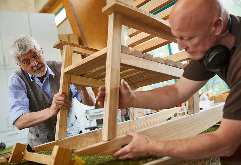 Der Tischler Schillings und sein Kunde Möllmann setzen die Einzelteile des Schaukelstuhls zusammen.