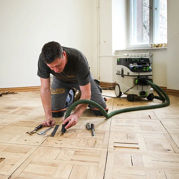 Parkettlegermeister Jarek Gawina löst defekte Teile aus dem Parkettboden und entfernt sie mit dem Festool Absaugmobil